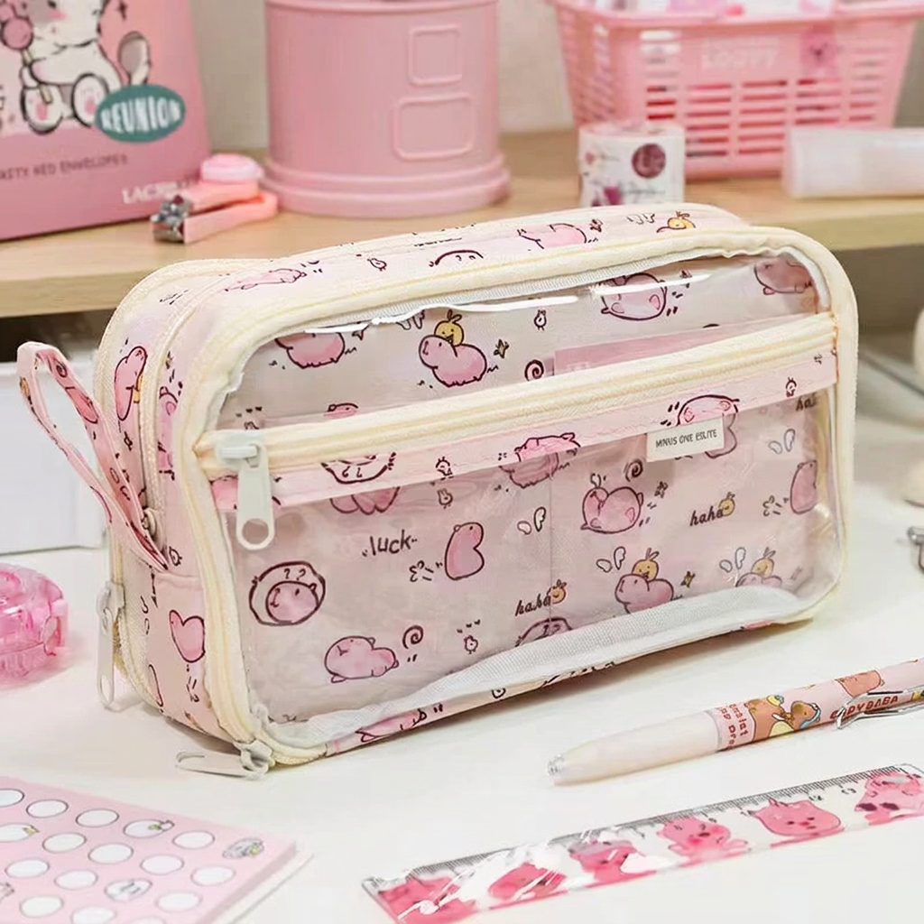 A pink cartoon-patterned pencil case with clear plastic front pockets, shown on a desk with stationery items and Chinese size text overlaid at the bottom.