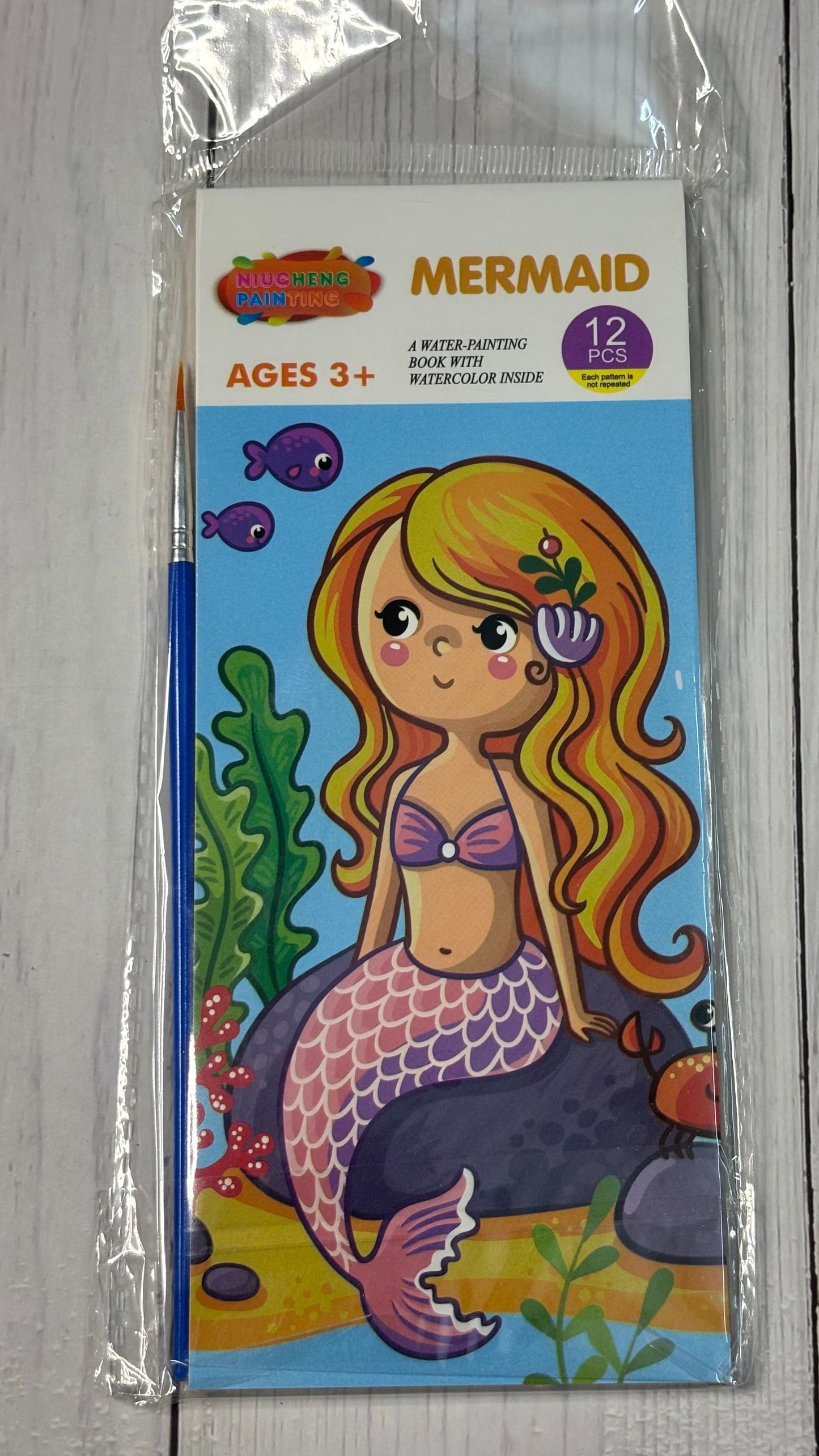 Mermaid-themed coloring book for ages 3+ in clear packaging on a gray surface