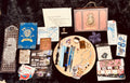 A styled flat-lay of Harry Potter themed stationery and accessories arranged on a black textured background. The collection includes a wooden tray with pens, stickers, and a bracelet, surrounded by books, cards, a notebook, and other themed items.