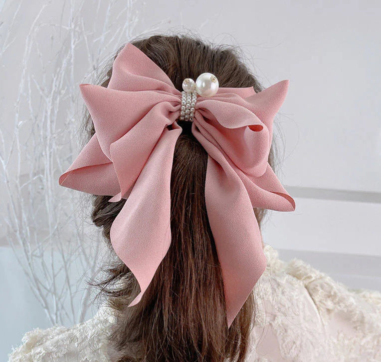 Large pink bow with pearls in a person's hair against a light background