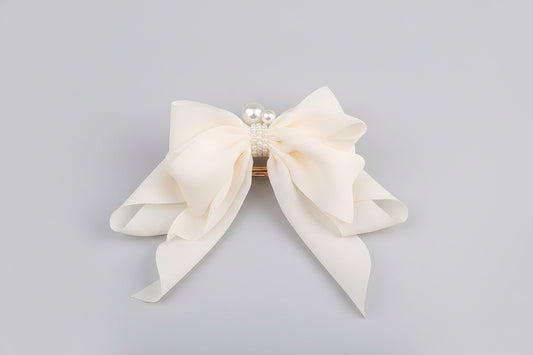 Large white bow with pearl accents held by a hand in an indoor setting.