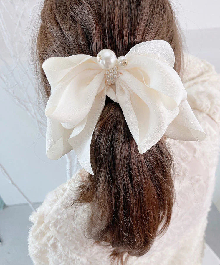 Large white bow with pearls in a person's hair, wearing a white coat.
