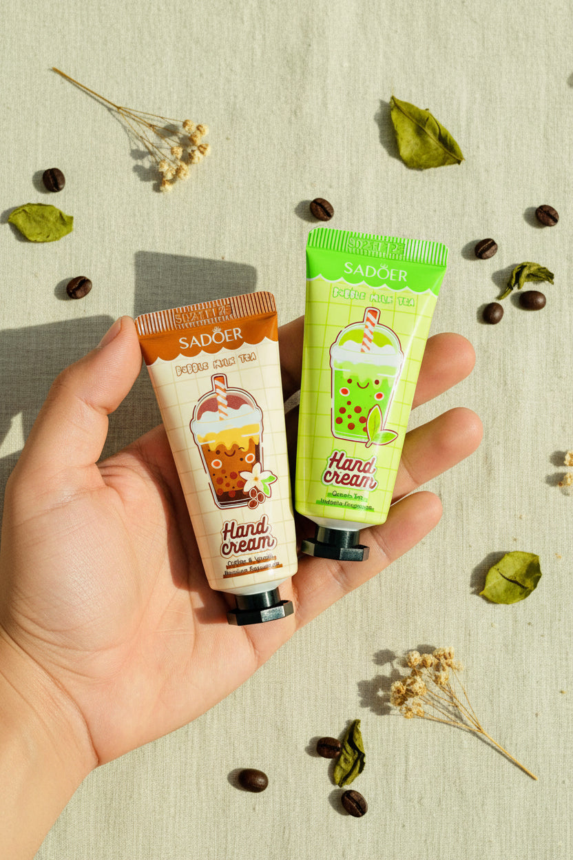 Two Sadoer bubble milk tea hand cream tubes held in a hand over a woven wicker background. One tube is orange-brown for Coffee Latte Tea, and the other is green for Green Milk Tea.