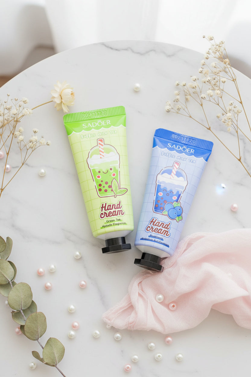 Two squeeze tubes of SADOER Bubble Milk Tea hand cream held in a hand against a woven wicker background. The left tube is light green for Green Tea flavor, and the right tube is light blue for Blueberry Milk Tea flavor.