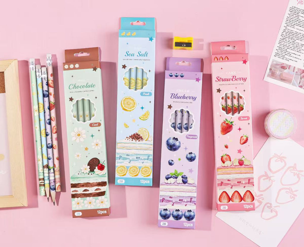 Four boxed 2B pencils in different flavors (Chocolate, Sea Salt, Blueberry, Strawberry) displayed on a pink background next to a gold pencil case and other stationery items. Chinese product specifications are printed at the bottom.