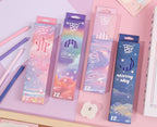 Four boxed HB pencils with pastel galaxy designs arranged on a pink desk, alongside loose colored pencils and stationery props. Chinese product text appears at the bottom with model, dimensions, weight, volume, quantity, and barcode.