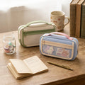 Two rectangular zippered toiletry/cosmetic cases shown on a white background, one in beige and sage green and one in light blue and cream with a pink handle.